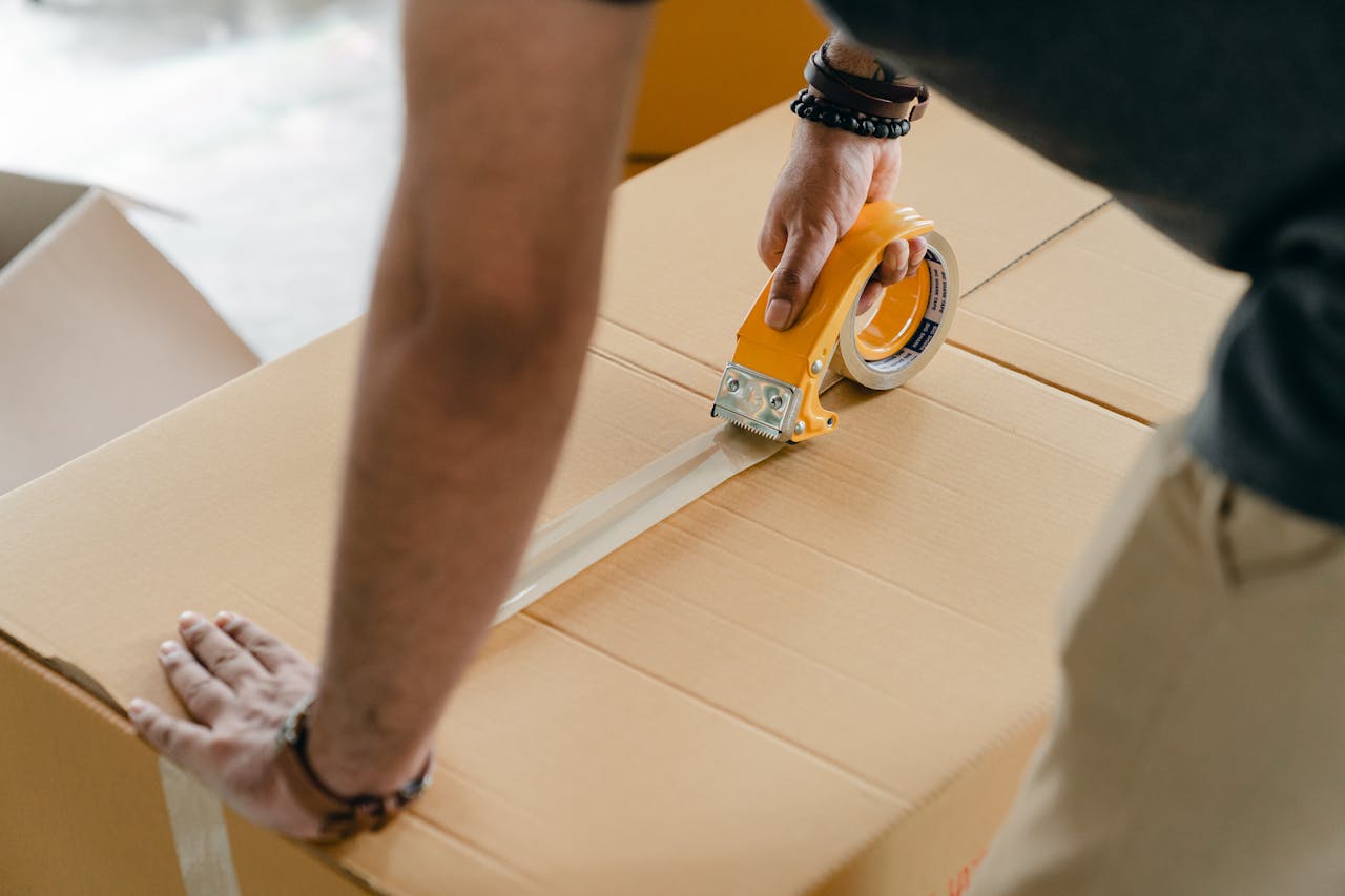 Home Man using packing tape to seal a cardboard box indoors. Ideal for moving or shipping concepts.