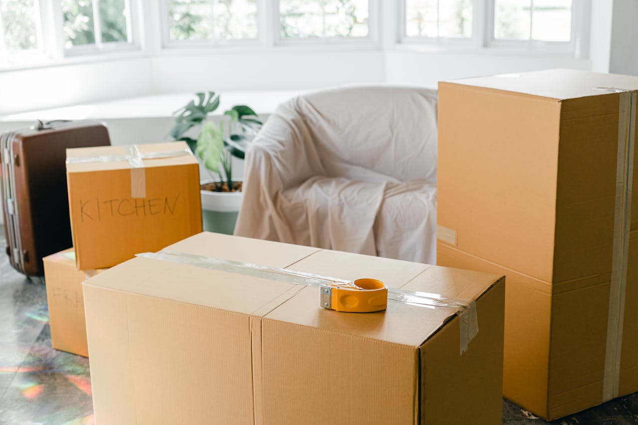 Contact Cardboard boxes labeled Kitchen in sunlit living room, ready for relocation.